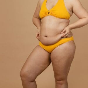 Cropped image of overweight woman, tucking, hiding fat naked big excessive belly in yellow pants