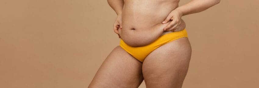 Cropped image of overweight woman, tucking, hiding fat naked big excessive belly in yellow pants