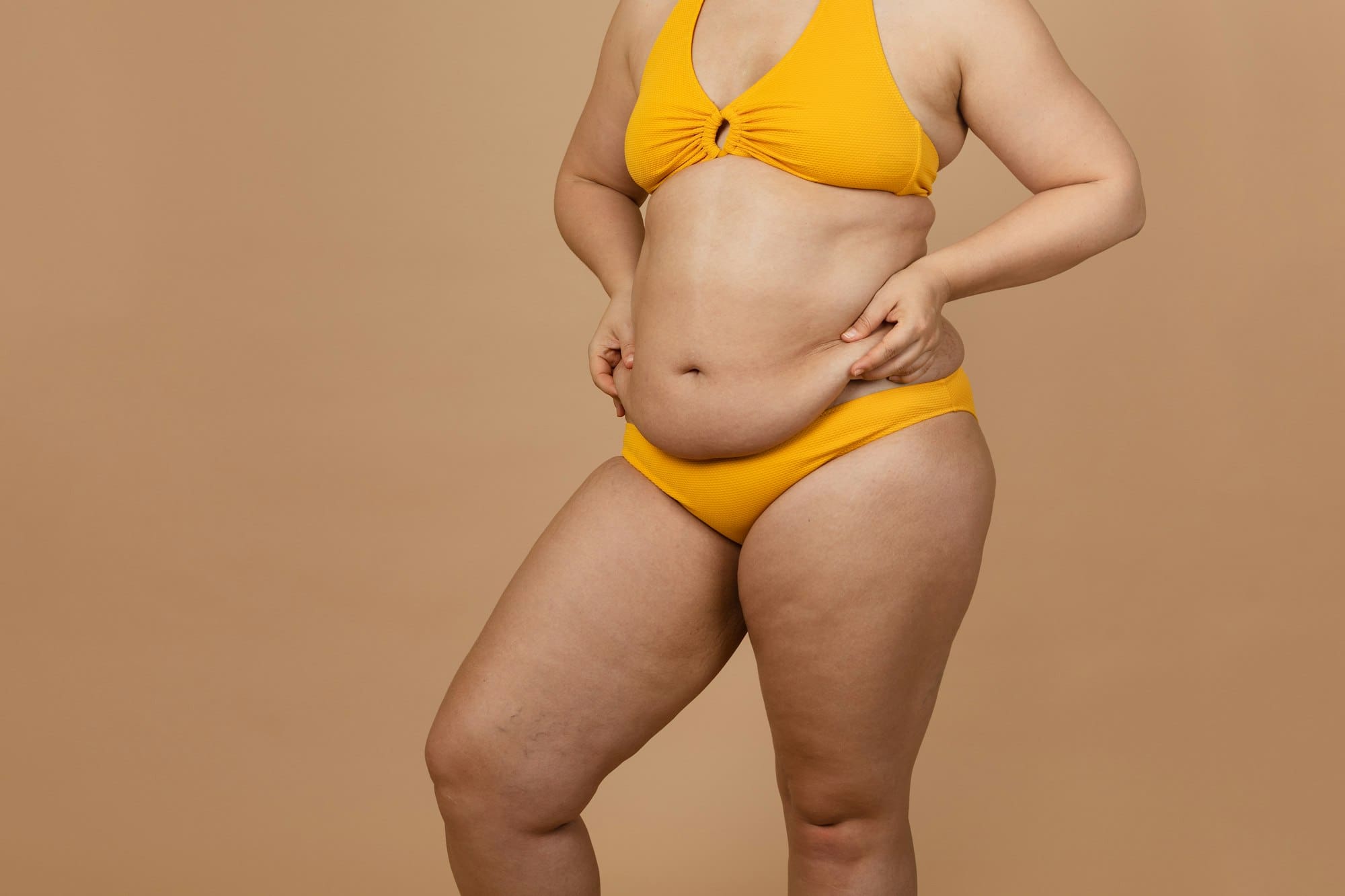 Cropped image of overweight woman, tucking, hiding fat naked big excessive belly in yellow pants