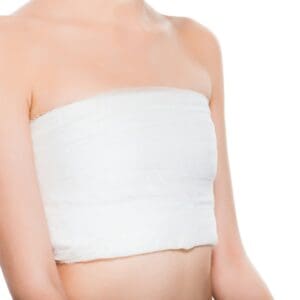 cropped view of young woman with bandaged breast after plastic surgery isolated on white