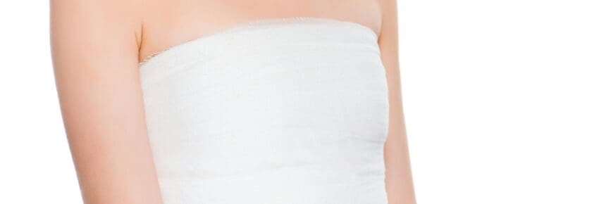 cropped view of young woman with bandaged breast after plastic surgery isolated on white