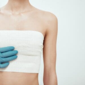 woman waiting for plastic surgery while surgeons in blue medical gloves measuring her breast