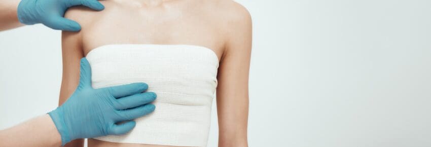 woman waiting for plastic surgery while surgeons in blue medical gloves measuring her breast