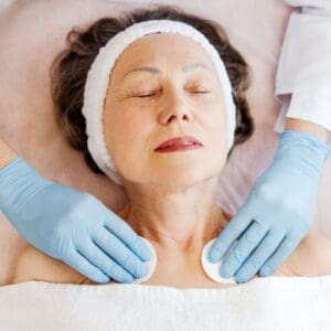 Mature woman lying in cosmetic clinic, doctor in latex gloves performing cosmetic procedures
