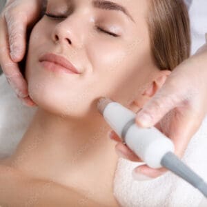 Close up of beautician hand making ultrasound facial procedure by special equipment. Her closed eyes with slight smile