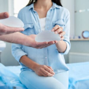 Doctor holding in his hands two silicone implants. Female patient trying to touch them