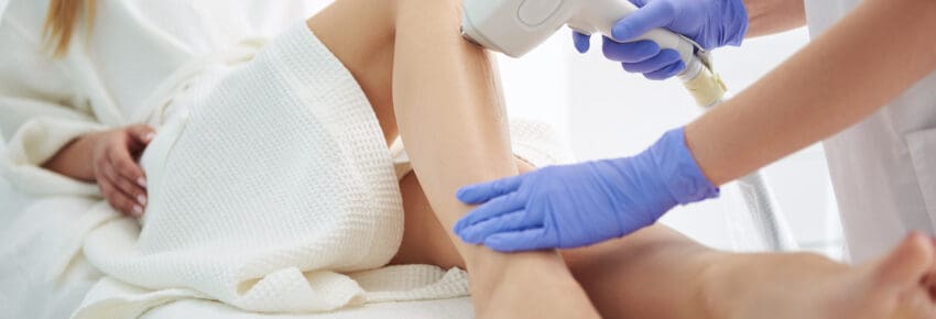 Young woman in white bathrobe receiving laser epilation in modern beauty salon